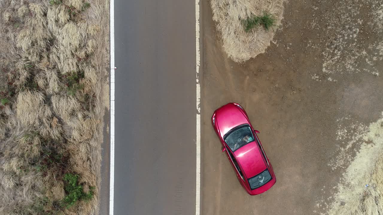 un auto rojo arranca al costado de la carretera y hacen girar sus neumáticos mientras se aleja.
