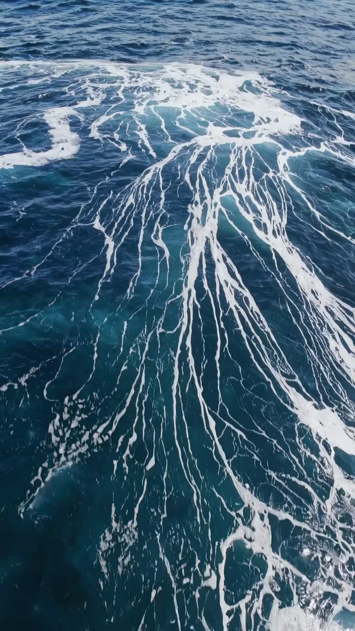 Aerial video captures swirling ocean currents with white foam patterns, showcasing dynamic movement