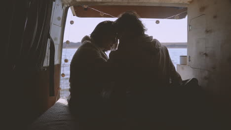 a young couple in love put their heads together in the back of a caravan by a lake 1