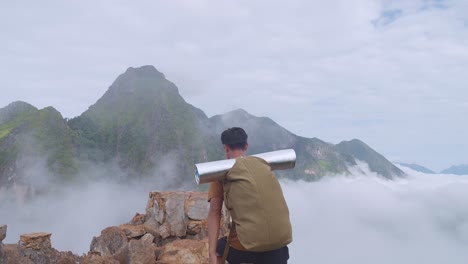 asian hiker male hiking to the top of foggy mountain and raising his hands for celebrating