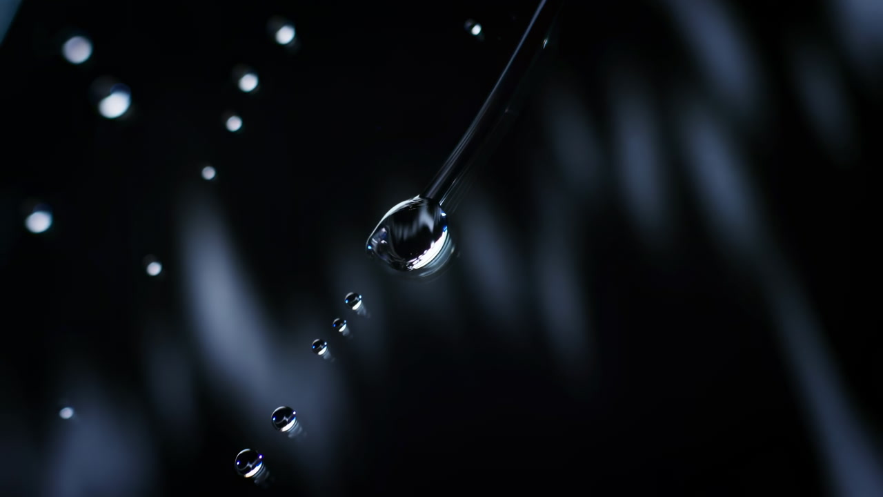 Dark Macro Shot Of Water Droplet On Pipette With Trailing Beads Suspended Against Deep Blue Black Background