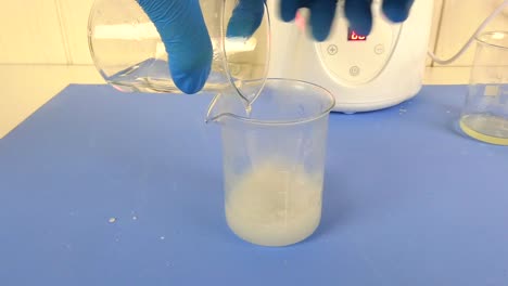 macro shot of a cosmetic emulsion being prepared in a laboratory. the video captures the operator's gloved hands mixing ingredients in a beaker,