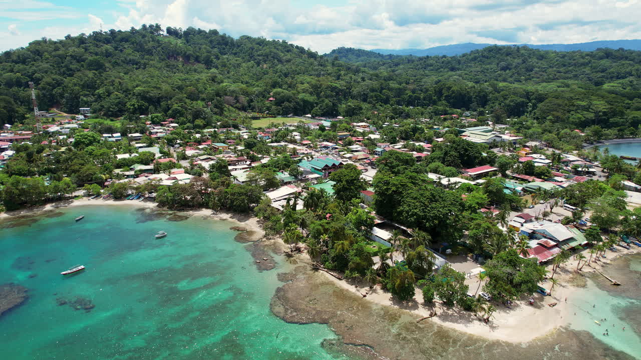 A wide circling aerial of tropical beaches, coral reefs and and lush mountains around the beach town of Puerto Viejo, a popular tourist destination on the Caribbean coast of Costa Rica.