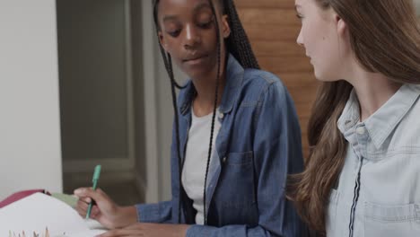 focused diverse teenage female friends studying and talking at table