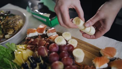 the girl puts the banana slices on a wooden tray on the table. she prepares delicious snacks for dinner