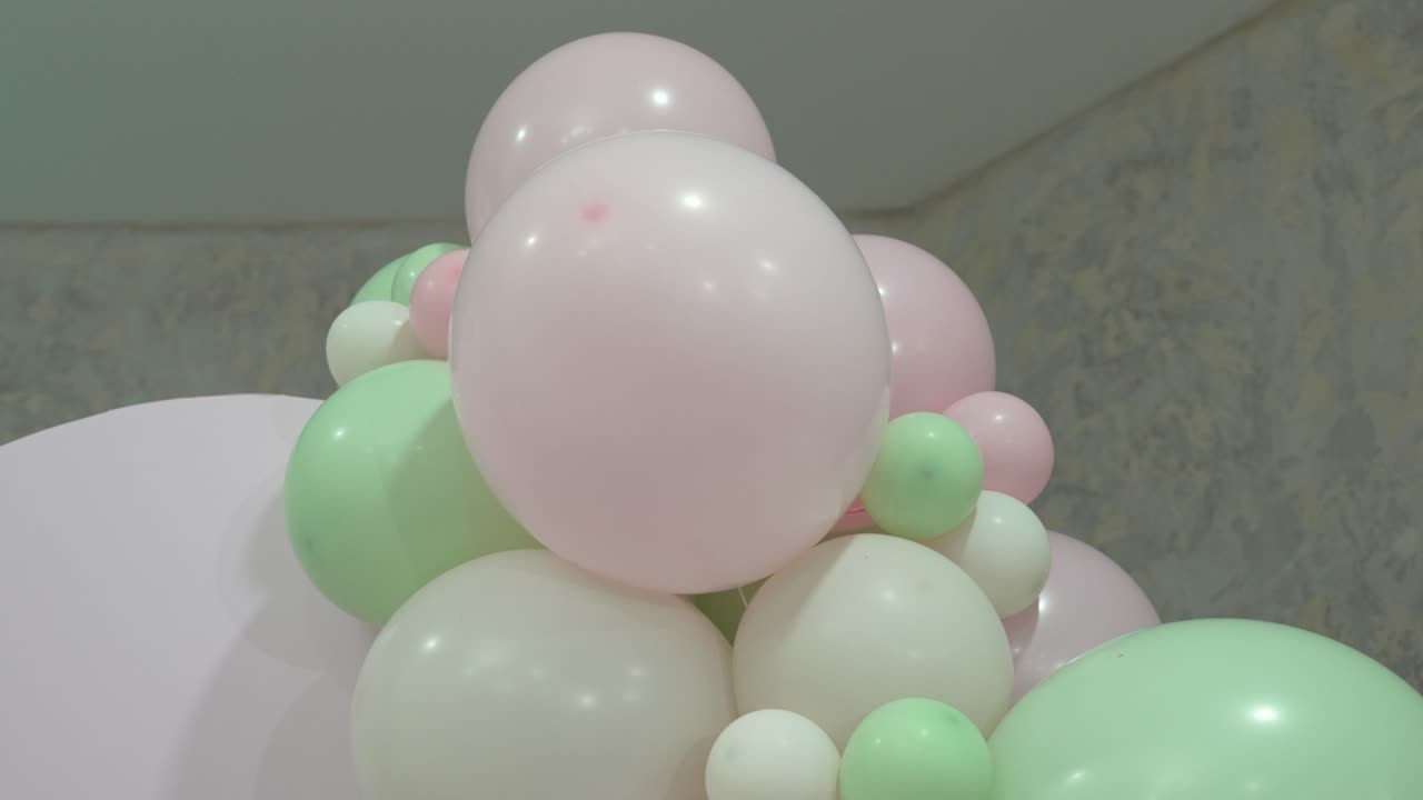 Palloncini nelle tonalità del rosa e del verde sono disposti insieme in uno spazio luminoso. Creano un'atmosfera festosa per una festa. L'area sembra pronta per l'arrivo degli ospiti.