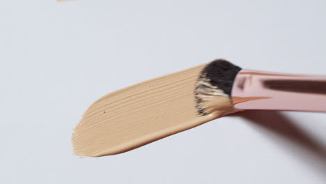 Brushing-a-wand-applicator-from-left-to-right,-loaded-with-a-nude-colored-foundation-on-a-clean-white-board-palette