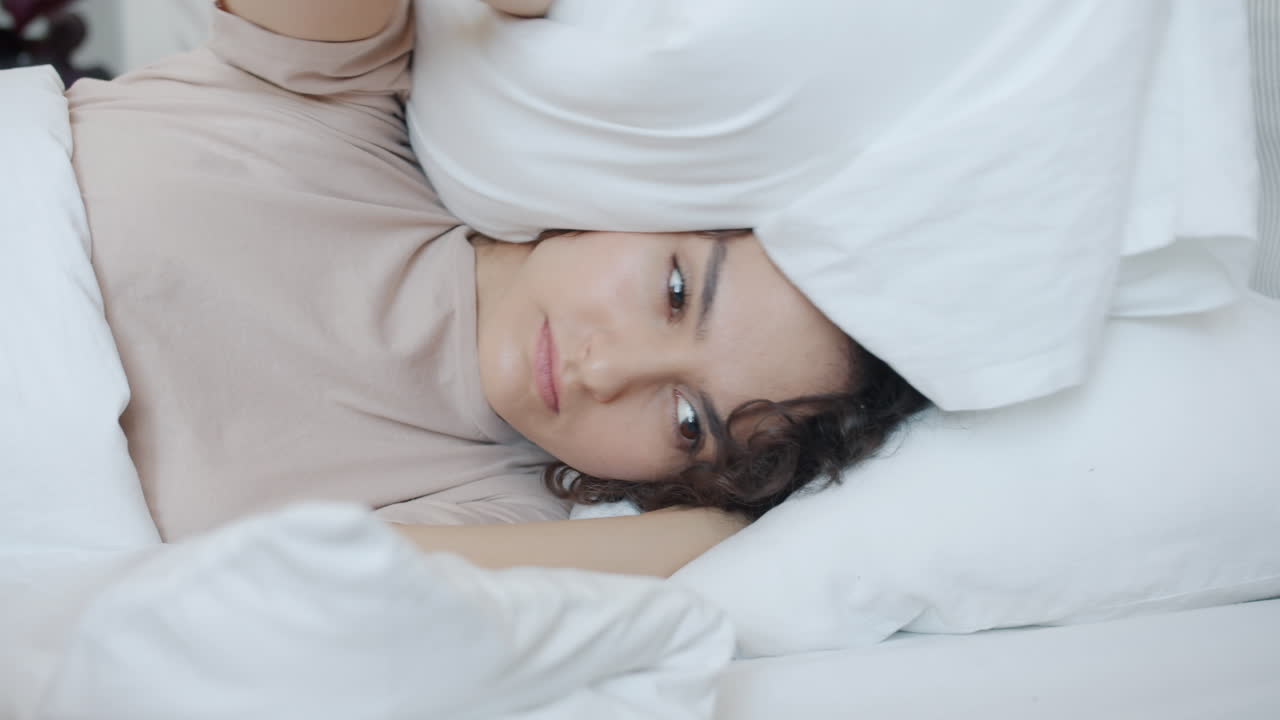 Woman covering her head with a pillow in bed