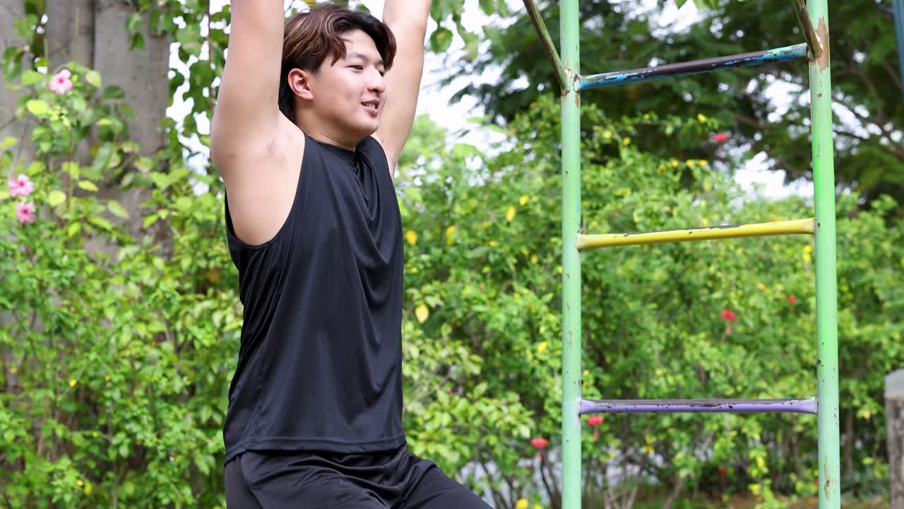 Seorang pria muda Asia yang bugar melakukan angkat kaki gantung di peralatan gym luar ruangan di Bangkok.