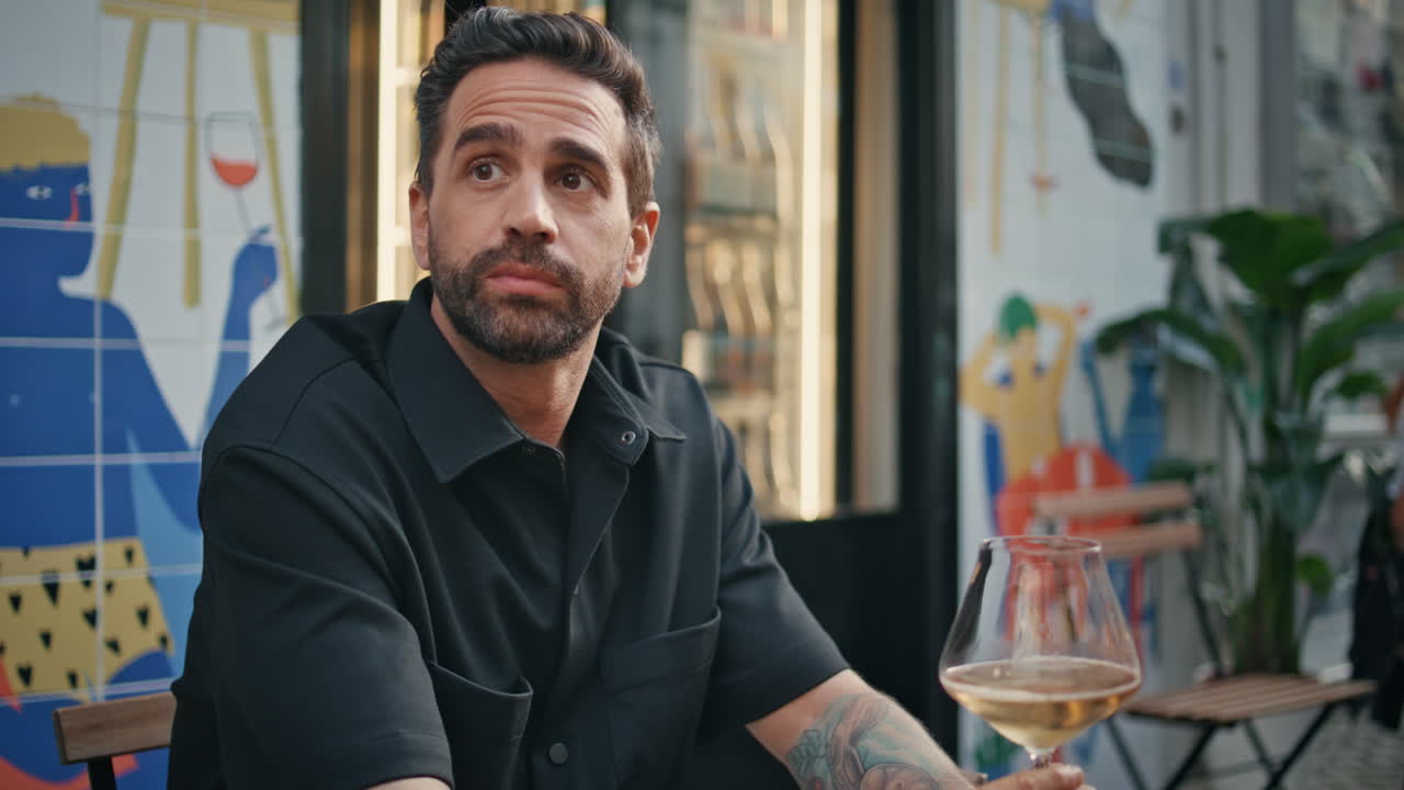 atractivo macho descansando alcohol restaurante callejero primer plano. hombre sosteniendo un vaso de vino