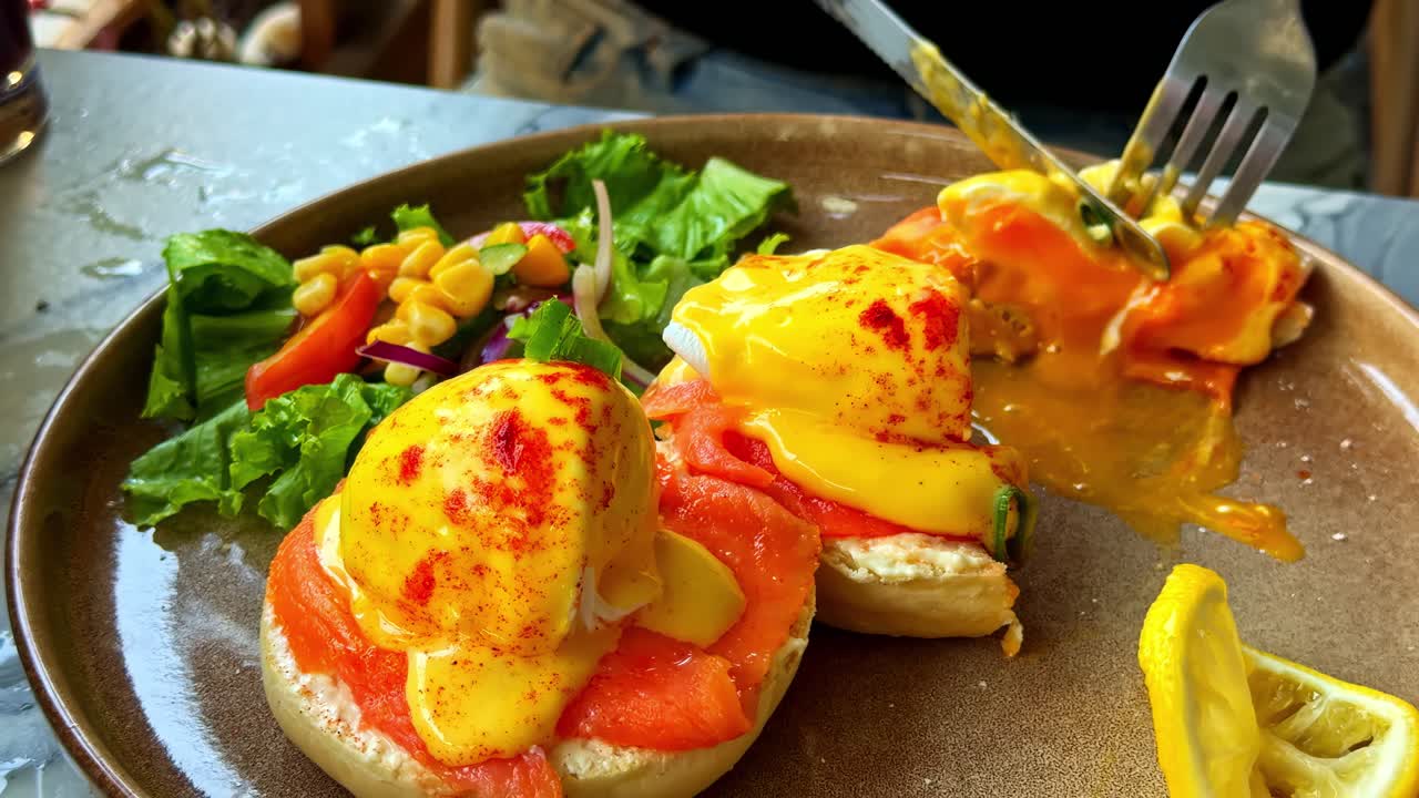Primo piano di una persona che mangia deliziose uova alla Benedict con salmone affumicato al mattino.