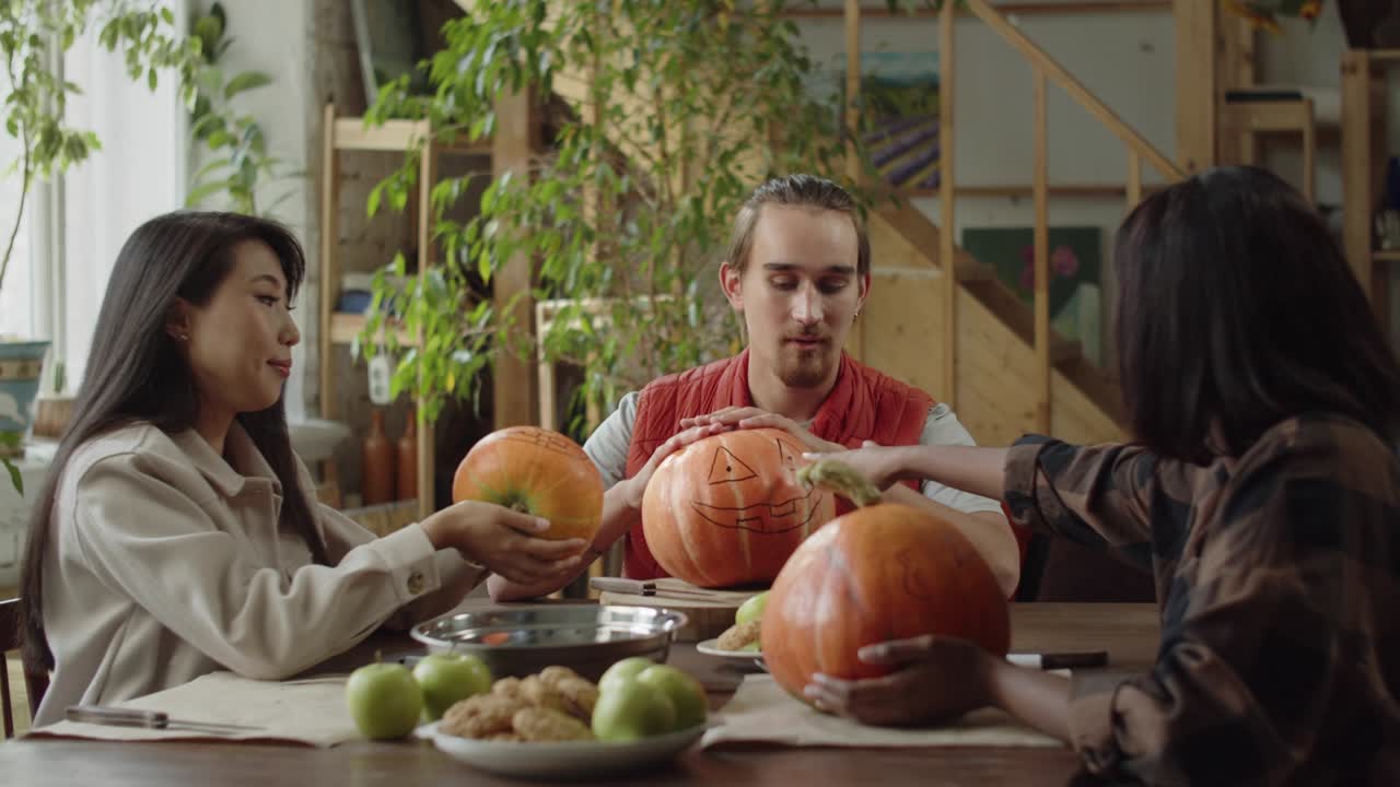 amigos están sentados en la mesa y comenzando a tallar calabazas para halloween juntos