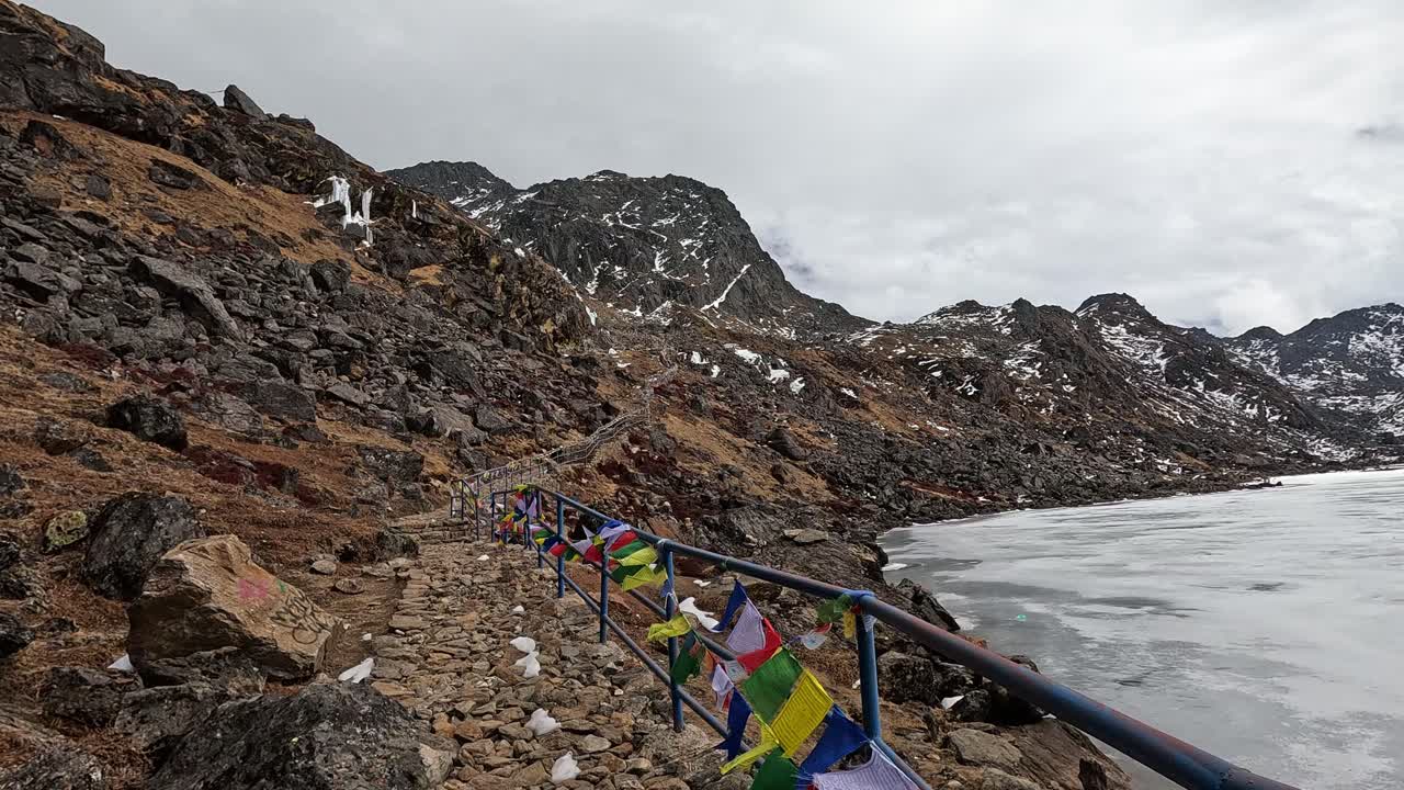sendero de senderismo con banderas de oración tibetanas y una barandilla en la orilla de frío y majestuoso: rocas de hielo y aguas heladas capturan la esencia de los himalayas en gosainkunda
