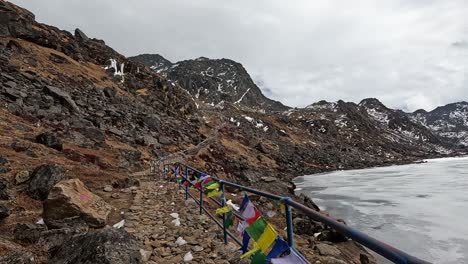 hiking path with tibetan prayer flags and a railing on the shore of cold and majestic: ice rocks and freezing waters capture the essence of the himalayas at gosainkunda