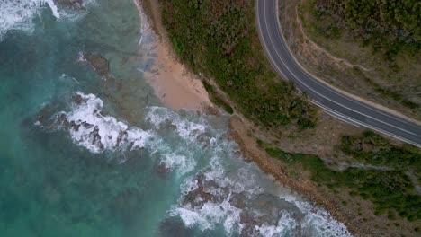 bird's eye drone view of great ocean road curved highway turn with white car and surf waves, victoria, australia