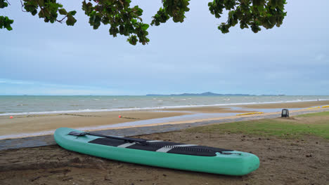 empty-paddle-board-on-beach-with-sea-background