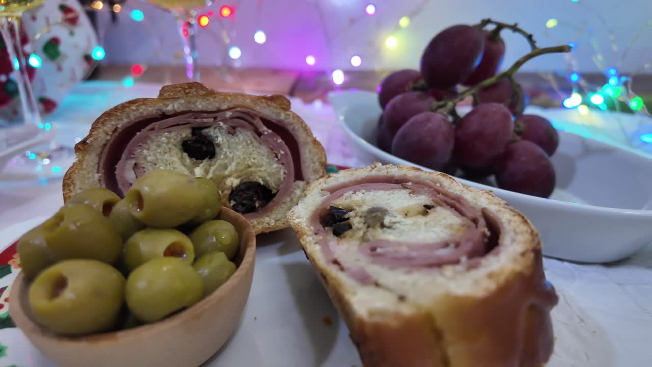 Festive ham-filled bread, olives, and grapes with holiday lights and cozy mood