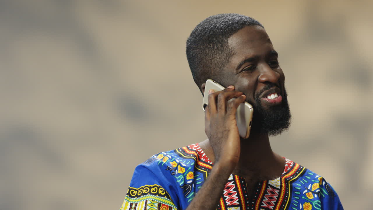 전통적인 옷을 입고 전화 통화를 하는 쾌활한 젊은 아프리카계 미국인 남자의 클로즈업 보기