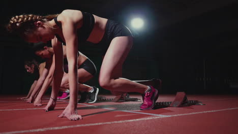 female runners at athletics track crouching at the starting blocks before a race. in slow motion.