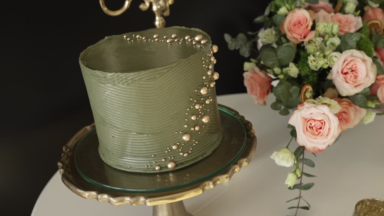 Close up of a modern green wedding cake with gold pearls on a stylish cake stand
