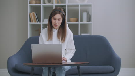 young woman wears headset conference calling on laptop talks with online teacher studying working from home. lady student e learning using computer webcam chat makes notes. distance education concept