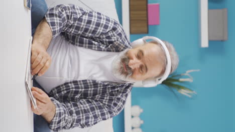 Vertical-video-of-Happy-old-man-listening-to-music-with-headphones.