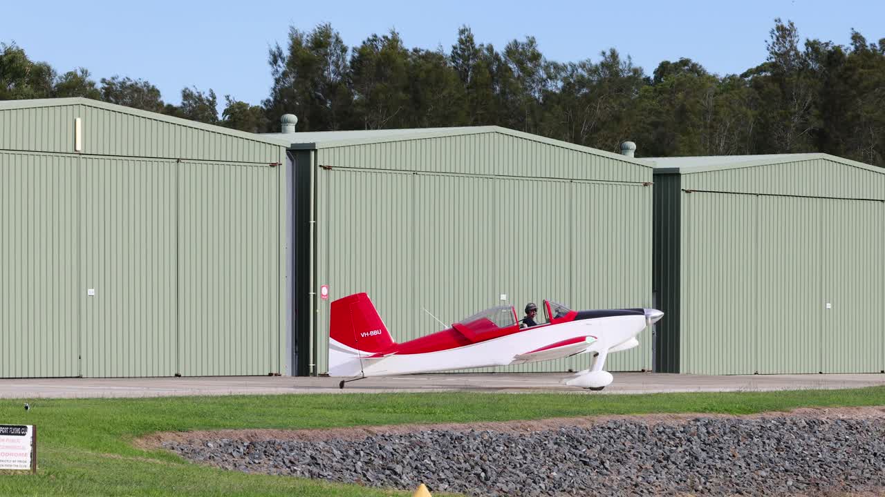 самолет ускоряется и взлетает рядом с зелеными ангарами.