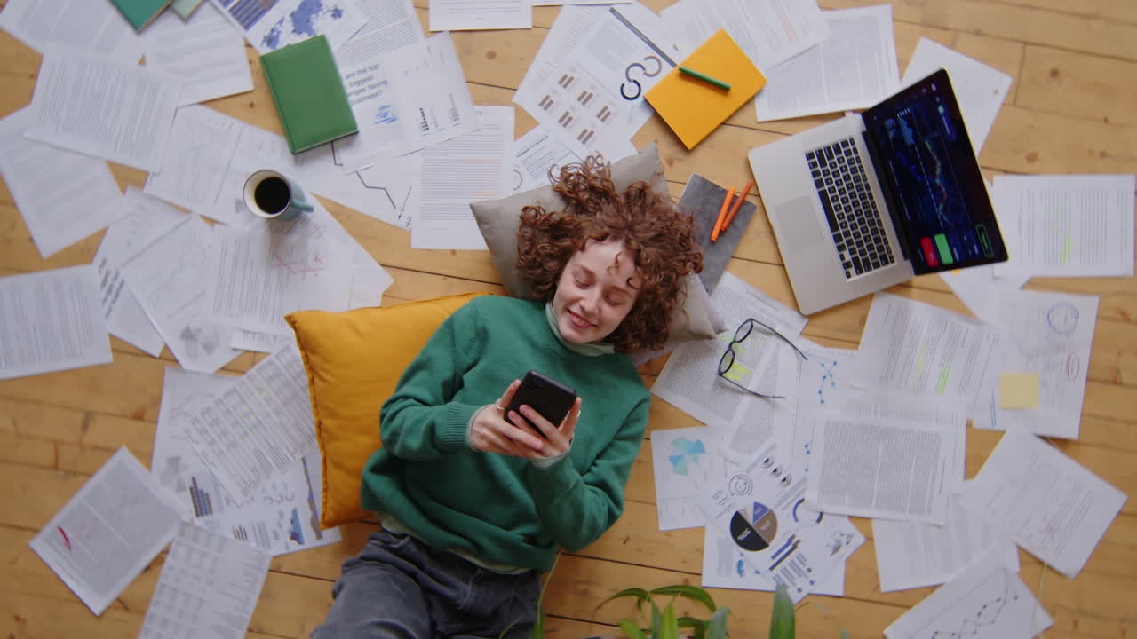 Female Freelancer Lying on Floor and Messaging on Phone