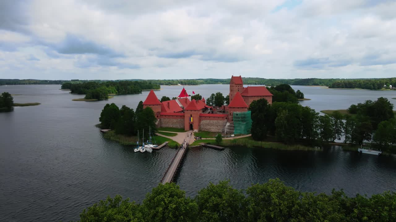 Ujęcie z drona przelatujące nad drewnianym mostem dla pieszych prowadzącym do wejścia do Zamku na Wyspie w Trokach na jeziorze Galwe.