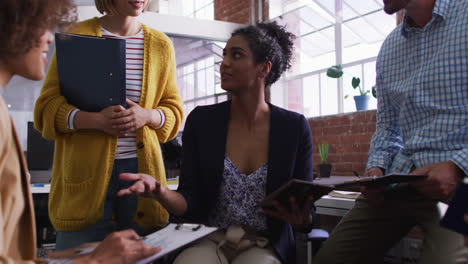 Mixed-race-businesswoman-using-tablet-in-office-discussing-with-diverse-colleagues