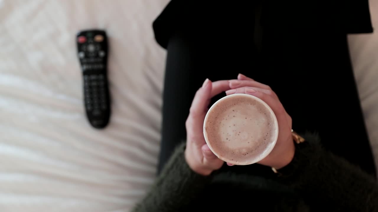 핫 초콜릿을 마시는 아늑한 여성이 tv를 켭니다.