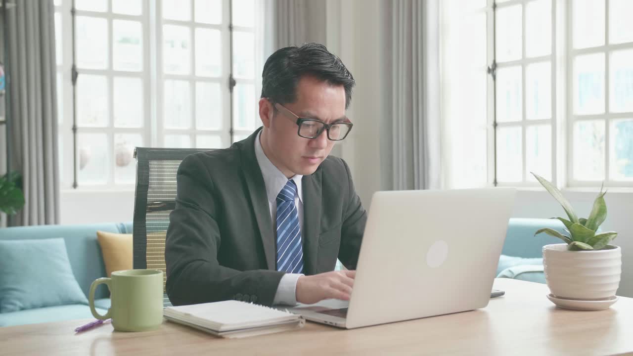 Asian Businessman With Glasses Wearing Business Suit Typing On Computer While Working At Home.