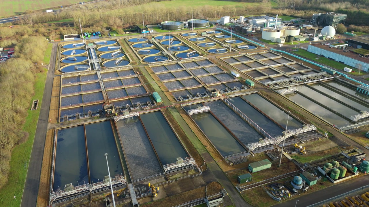Drone view of symmetrical sedimentation tanks and sewage processing infrastructure at a major Milton Keynes water recycling facility, showcasing modern engineering and sanitation systems.