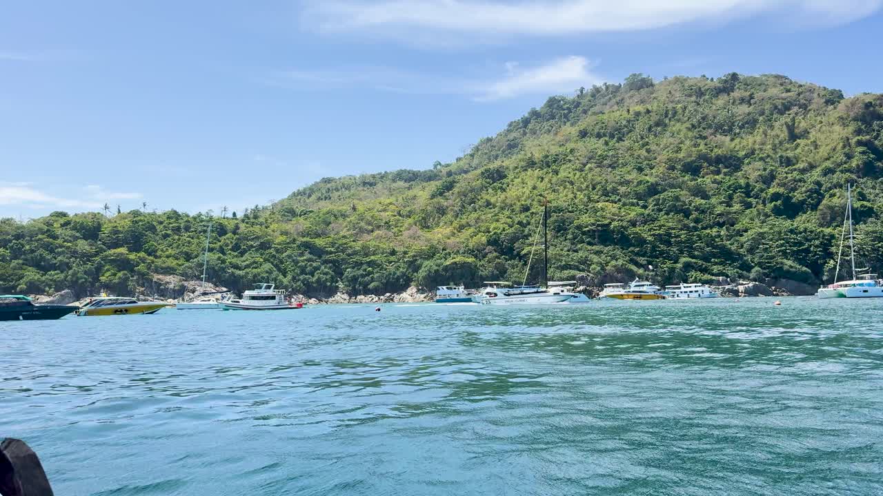 A serene boat journey across Chalong Bay, capturing lush green hills and clear blue waters under bright daylight