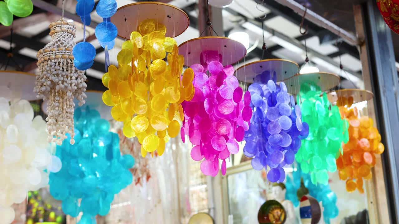 Colorful shell decorations sway gently in a Phuket market, showcasing vibrant hues and intricate designs under natural lighting
