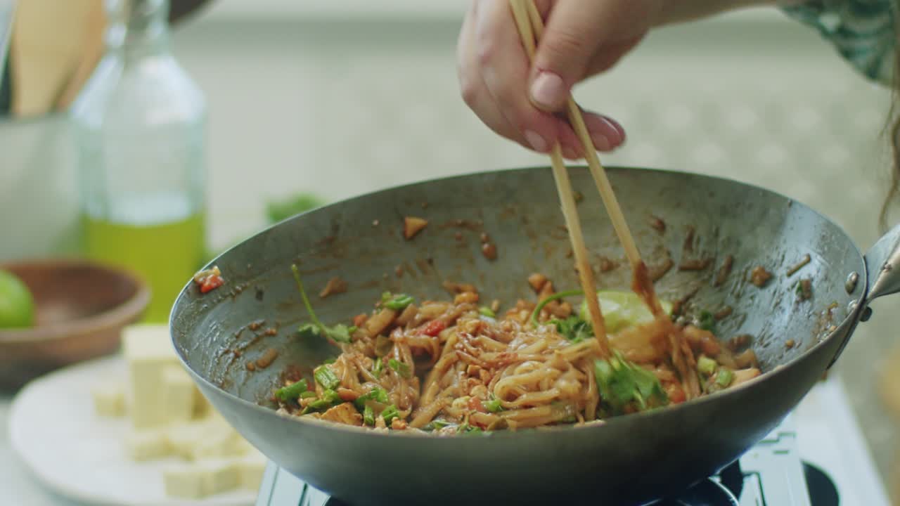 Woman mixing delicious wok noodles with chopsticks