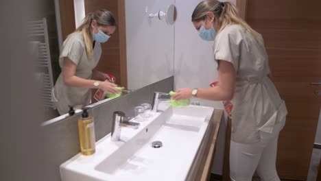 cleaning lady with face mask cleans the washbasin in a hotel room