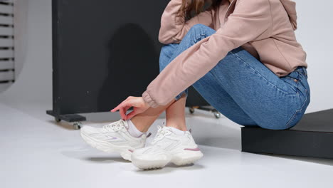 cropped image of a girl sitting on a black step. model in jeans, sweatshirt and white sneakers in studio.