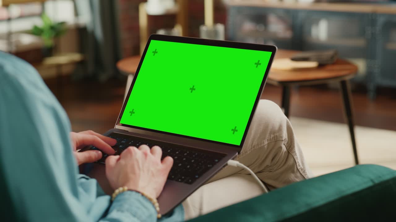 Young Adult Man Working from Home Loft Apartment on Laptop Computer with Green Screen Mock Up Display. Creative Male Browsing the Web, Writing on Social Media. Close Up Over the Shoulder Footage.