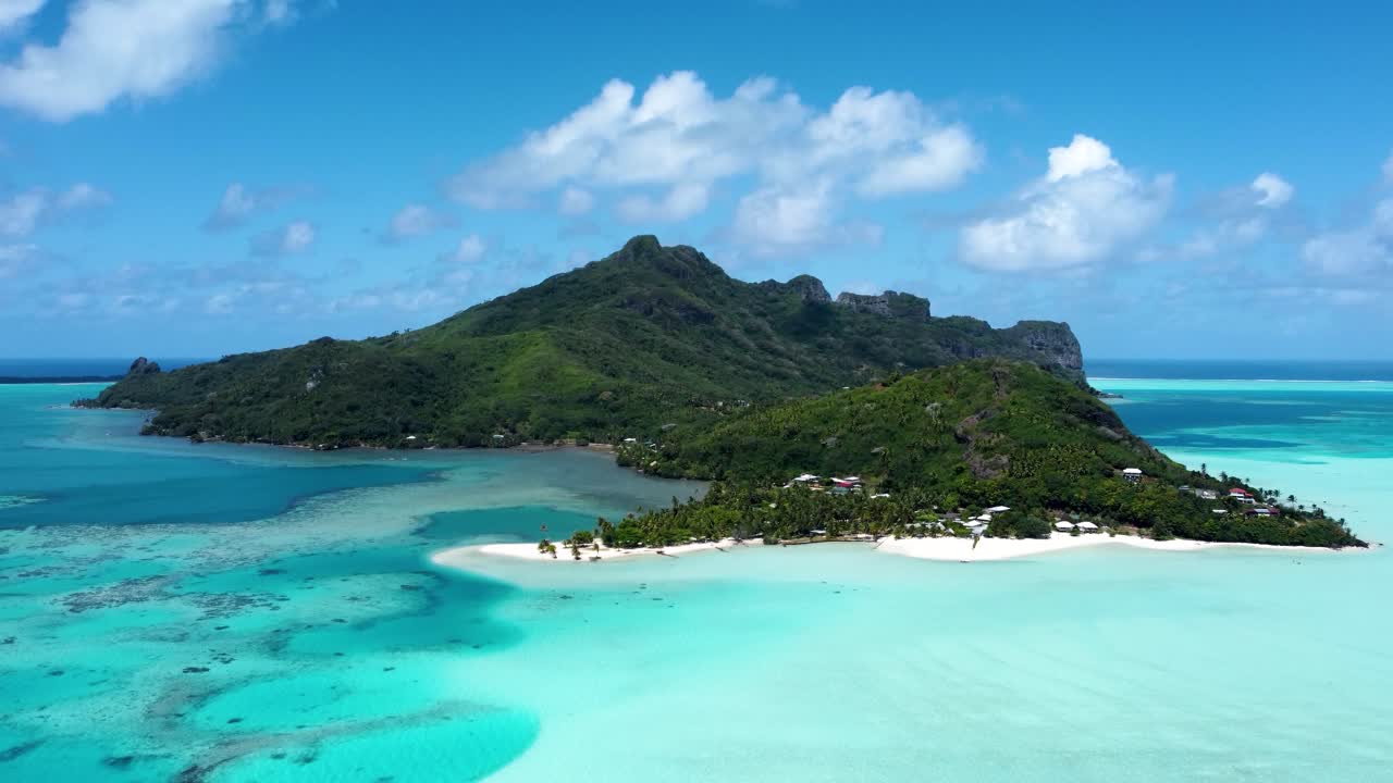 Drone view of a small green tropical pacific island with blue shallow water and a lagoon on a sunny day in Maupiti, French Polynesia.