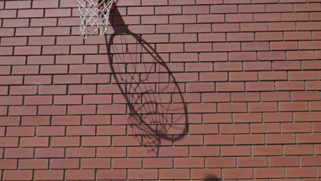 front on slow motion shot of basketball net silhouette shadow as ball goes into ring scoring goal on red brickwork wall