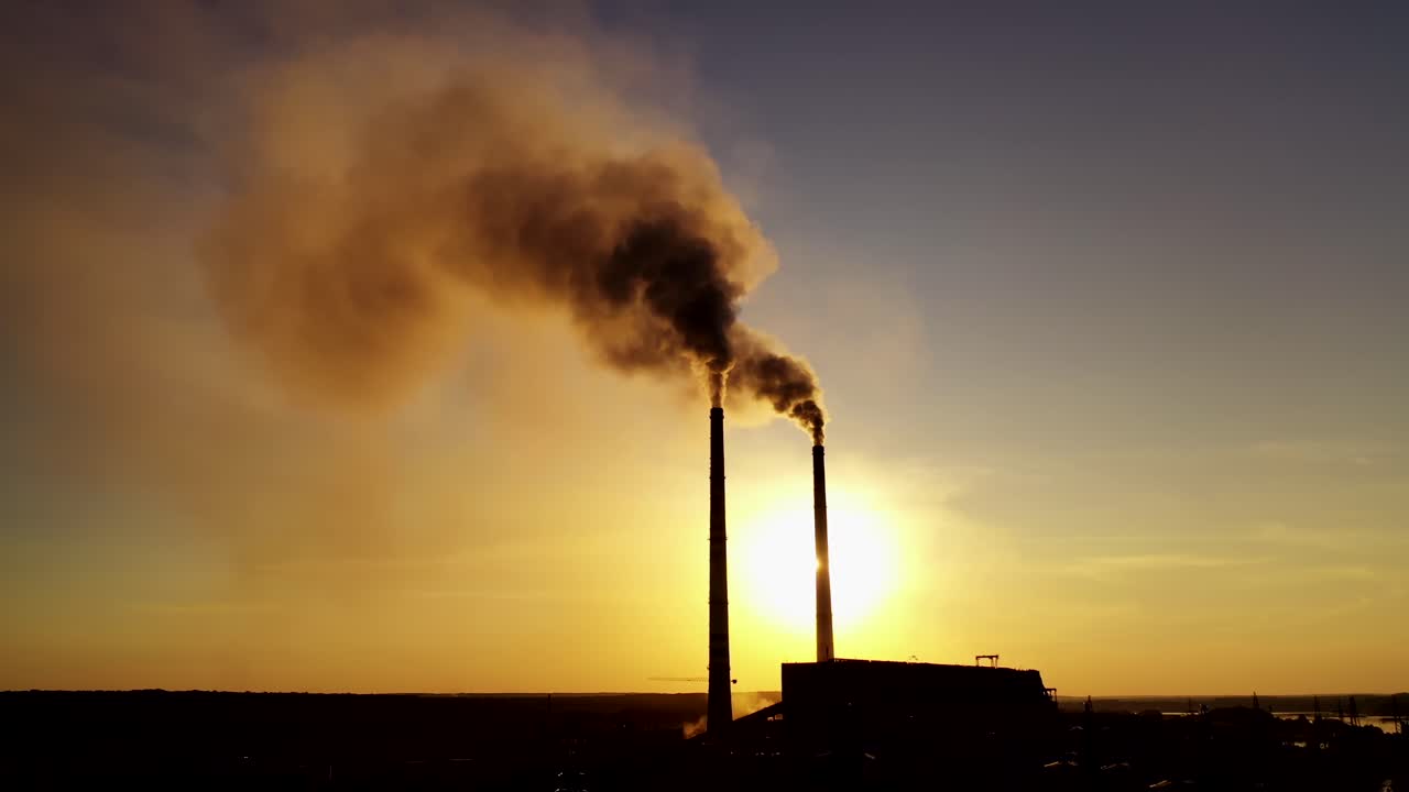 Dark silhouette of a factory at sunset. Pipes with dirty smoke of metallurgical plant in the evening.