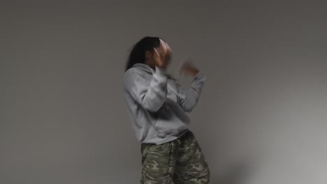 studio portrait shot of young woman wearing hoodie dancing with low key lighting against grey background