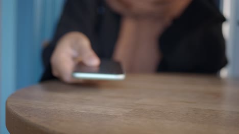 mujer sentada en una mesa de café, sosteniendo un teléfono inteligente verde