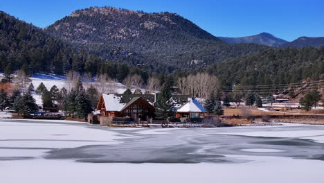 first snow ice frozen covered white evergreen lake house rocky mountain landscape scene morning front range denver aerial cinematic drone christmas ice skating hockey blue sky right motion