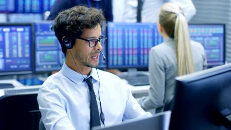 stock trader making sales with a headset. in the background stock exchange office and group of traders working at their workstations.