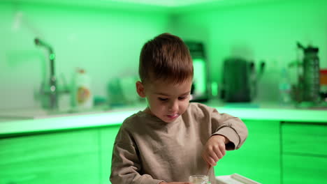smiling caucasian baby sitting in the kitchen. kid takes a bite of a bun and eats some yogurt. blurred backdrop.