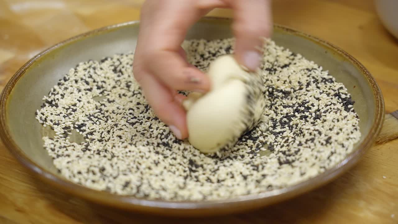 Hand dipping dough into sesame seeds for baking