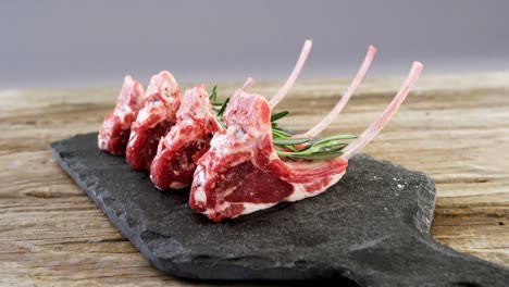 chuletas de carne cruda y romero dispuestas en la bandeja de piedra