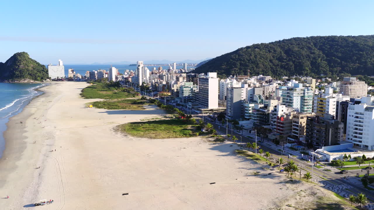 Left panning drone movement from the Caiobá Brazilian beachfront with high-rise buildings and green hills in background, Matinhos, Paraná, Brazil